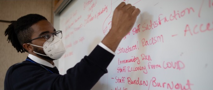 A doctor writes notes in red ink on a whiteboard.